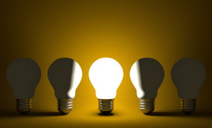 Glowing light bulb in row of switched off ones on yellow. Front view