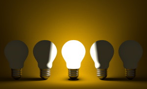 Glowing light bulb in row of switched off ones on yellow. Front view