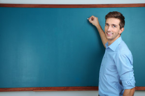 Young teacher near chalkboard in school classroom